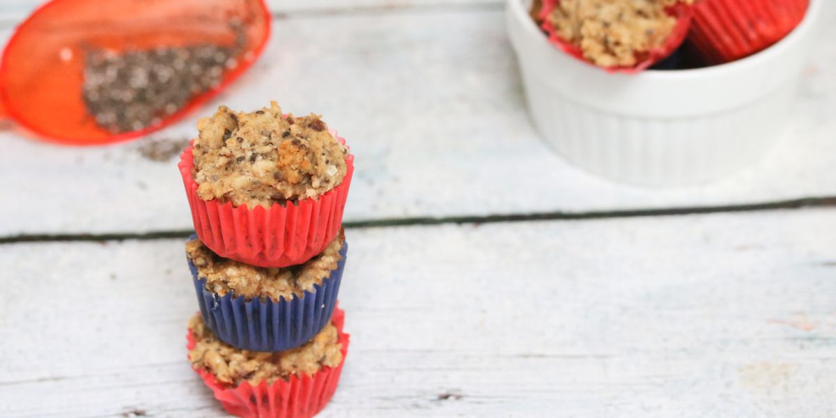 Three bite-sized toddler muffins stacked on top of each other with a toddlers hand reaching for them.