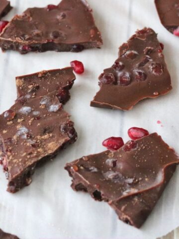 chocolate pomegranate bark broken up on parchment paper with pomegranate seeds around it.