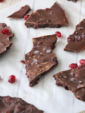 Chocolate pomegranate bark broken up on parchment paper with pomegranate seeds around it.