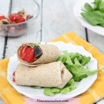 Featured image: two veggie wraps on a white plate with lettuce with grilled vegetables and salad behind it and a yellow linen under it
