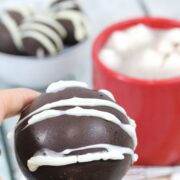 How chocolate bomb with white icing being held between two fingers.