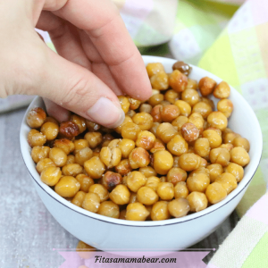 Featured image with text: salt and vinegar roasted chickpeas in a white bowl with a hand grabbing for them