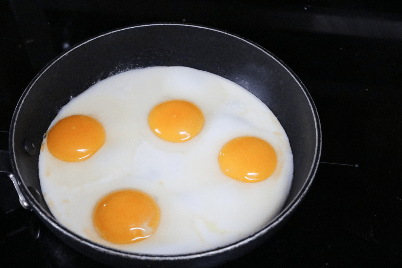 Black pan on a black stove with four eggs being cooked in it