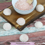 featured image with text: DIY exfoliating salt lotion bars on and around a wooden cutting board with a white bowl of pink salt and a wooden spoon in it