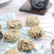 Paleo breakfast cookies on a cooling rack on a blue linen with plates and chocolate chips around them.