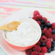 Pink bowl with whole30 whipped cream and a wooden spoon in it and berries on the side of a white plate.