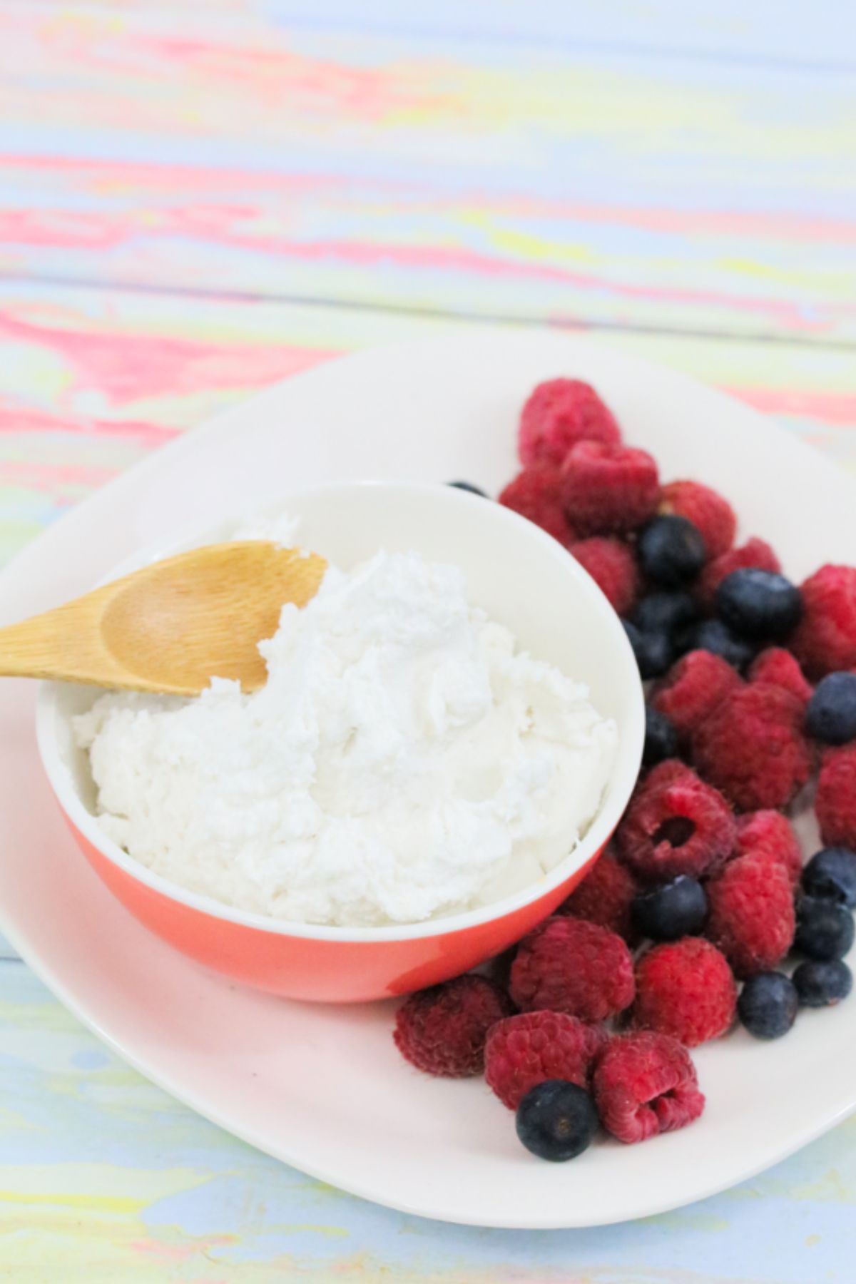 Pink bowl with whole30 whipped cream and a wooden spoon in it and berries on the side of a white plate.