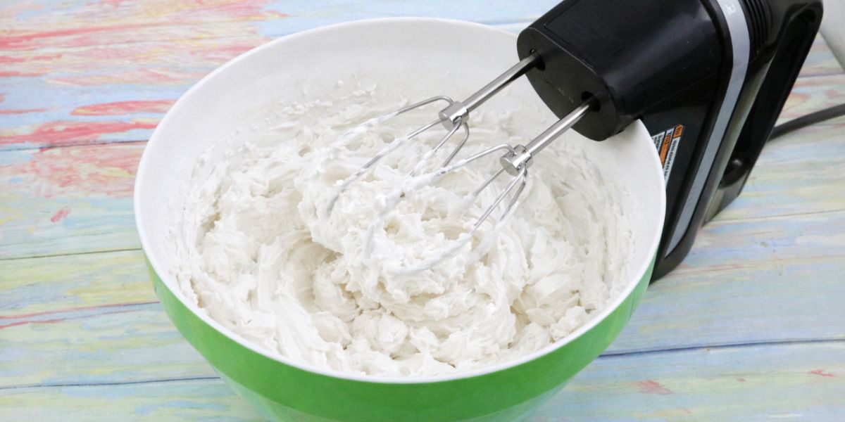 Whole30 whipped cream in a green bowl with a hand mixer.