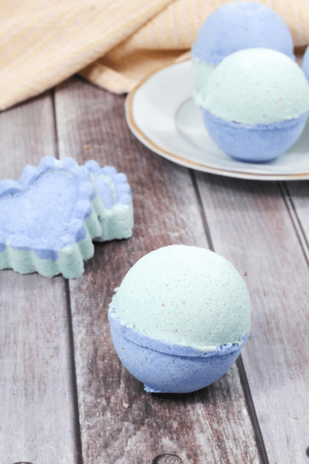 Blue and green bath bomb with heart shaped bath bombs and more bath bombs on a white plate behind it