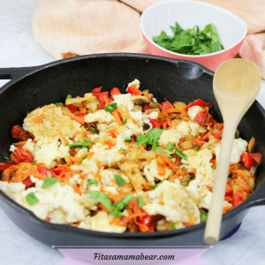Featured image with text: cast iron pan with veggie and egg scramble and a wooden spoon on the side, eggs behind it