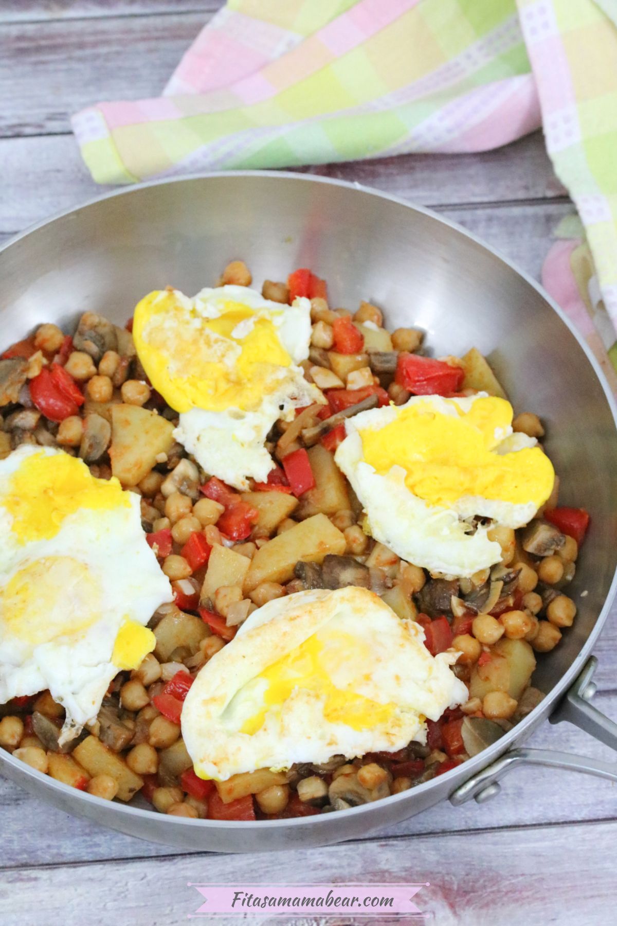 Breakfast hash with red peppers, chickpeas, potatoes, and eggs in a steel pan.