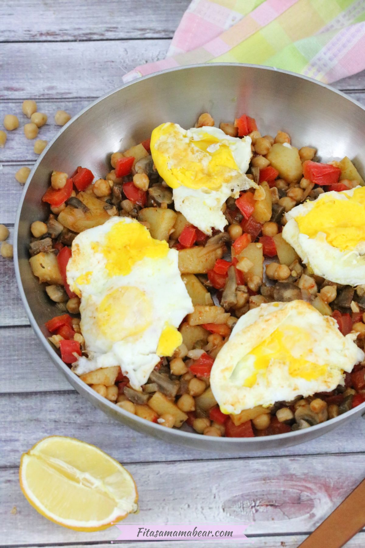 Breakfast hash with red peppers, chickpeas, potatoes, and eggs in a steel pan.