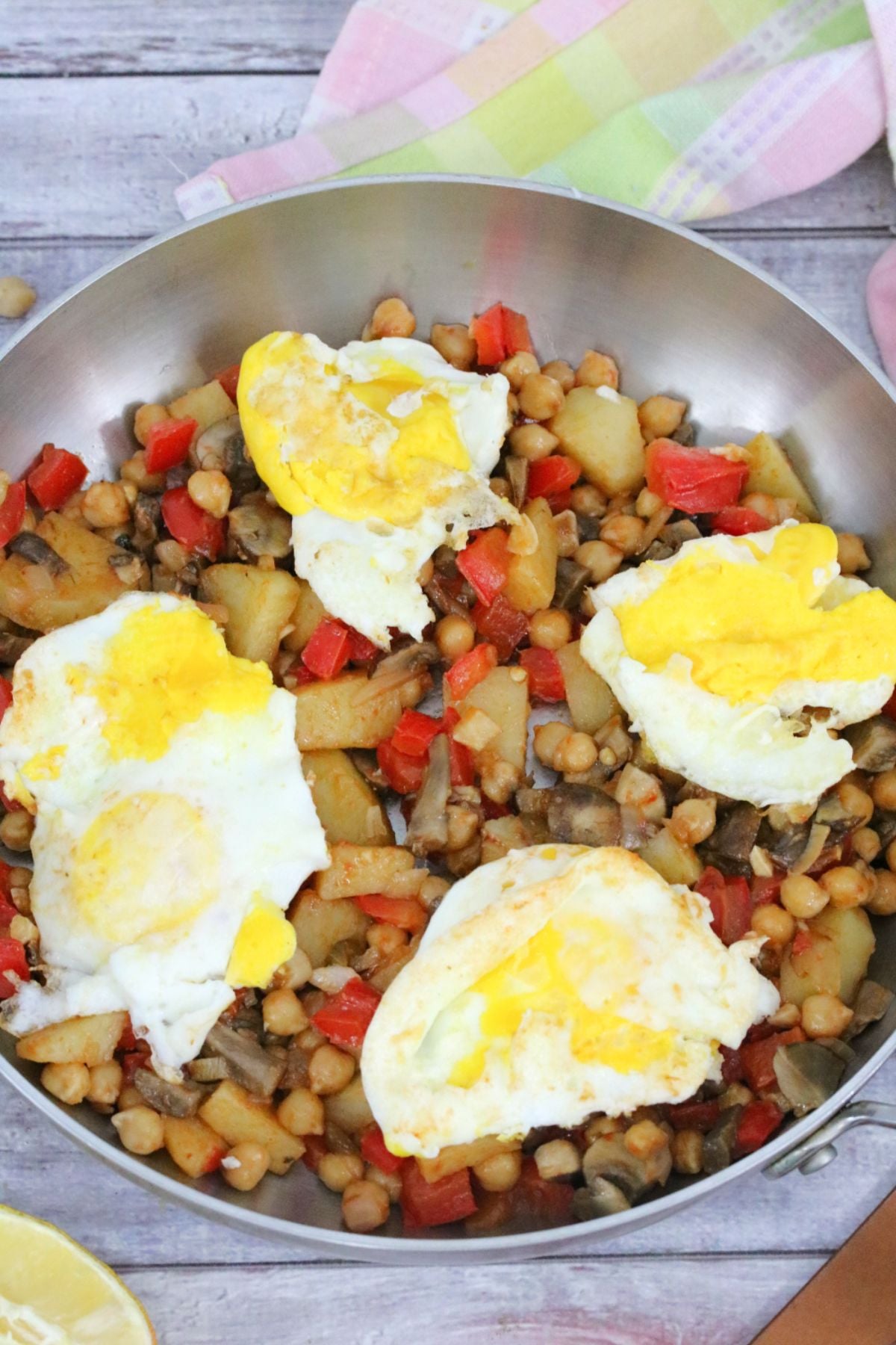 Breakfast hash with red peppers, chickpeas, potatoes, and eggs in a steel pan.