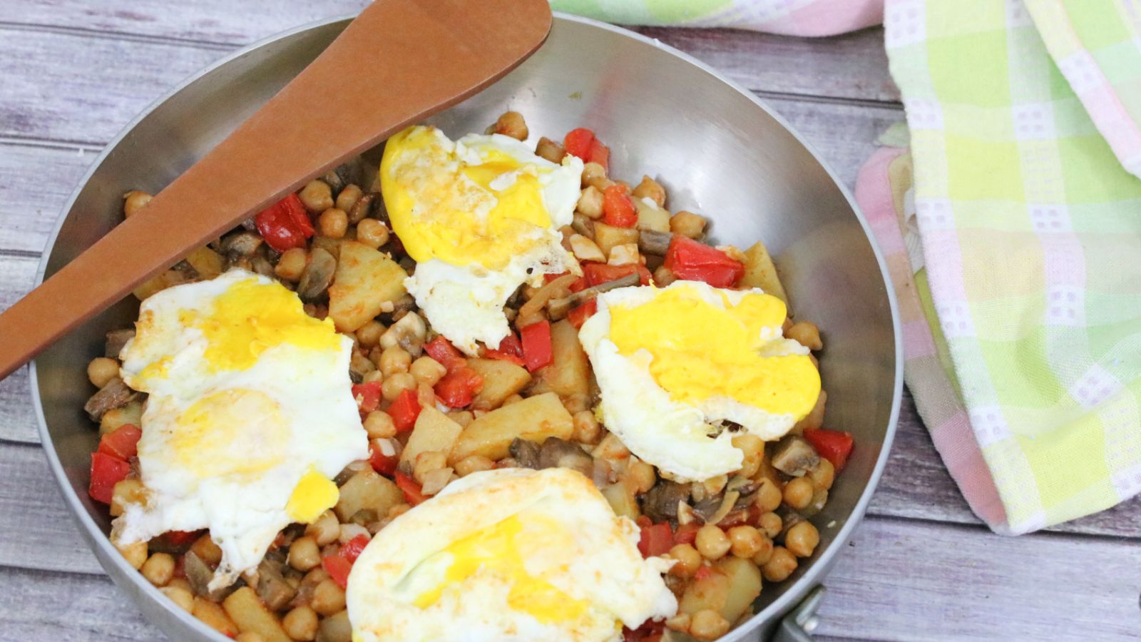 Breakfast hash with red peppers, chickpeas, potatoes, and eggs in a steel pan.
