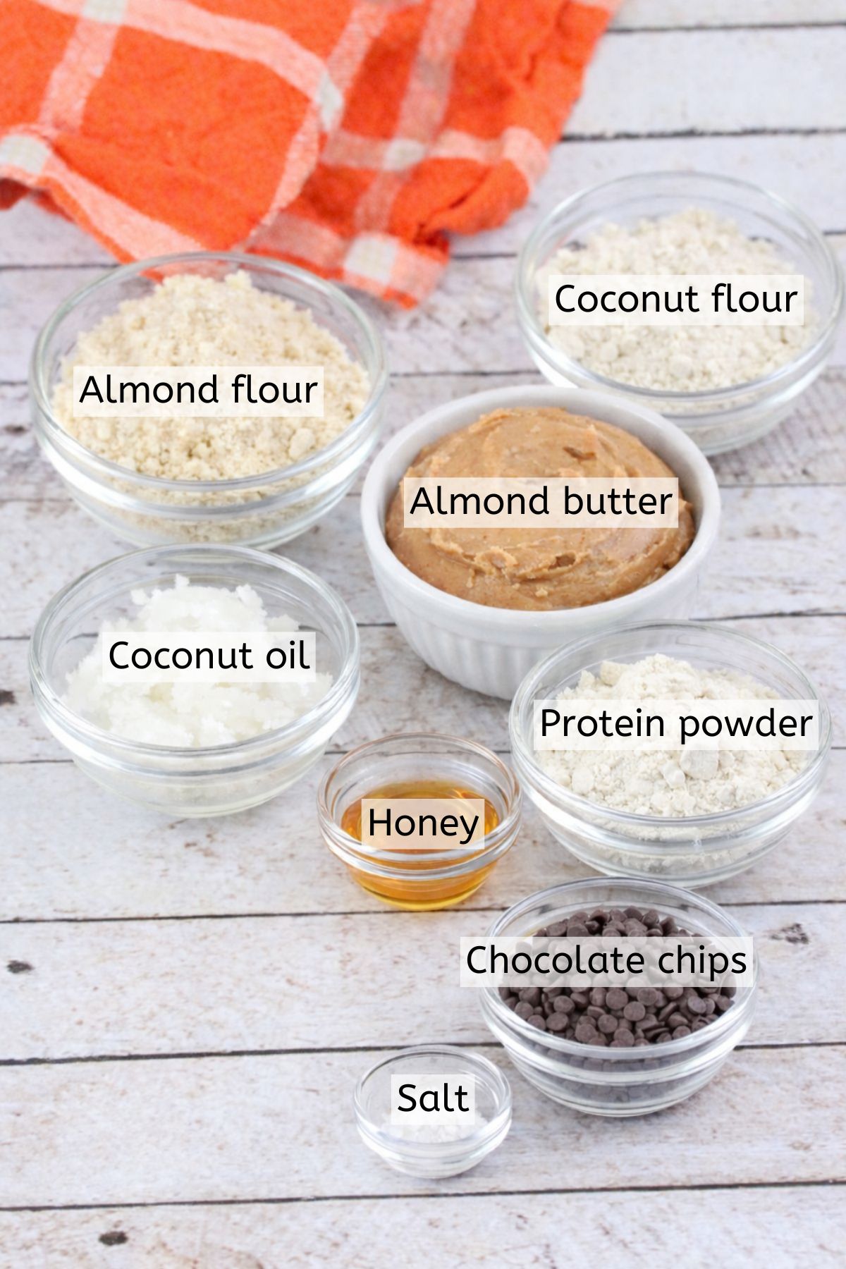 Almond butter, flours, protein powder, and more in glass bowls with text labels over top.