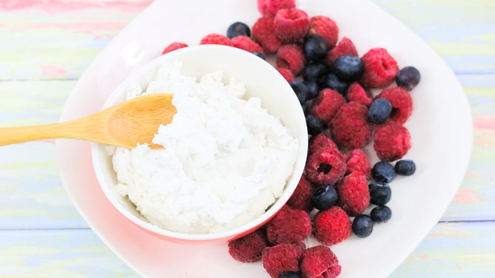 Coconut whipped cream in a bowl with a wooden spoon and berries on the side.