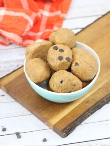 paleo cookie dough ball being held between fingers with more in a bowl