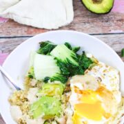 White bowl with quinoa, avocado, over easy eggs, and bok choy with avocado behind it.