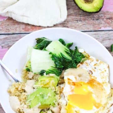 White bowl with quinoa, avocado, over easy eggs, and bok choy with avocado behind it.