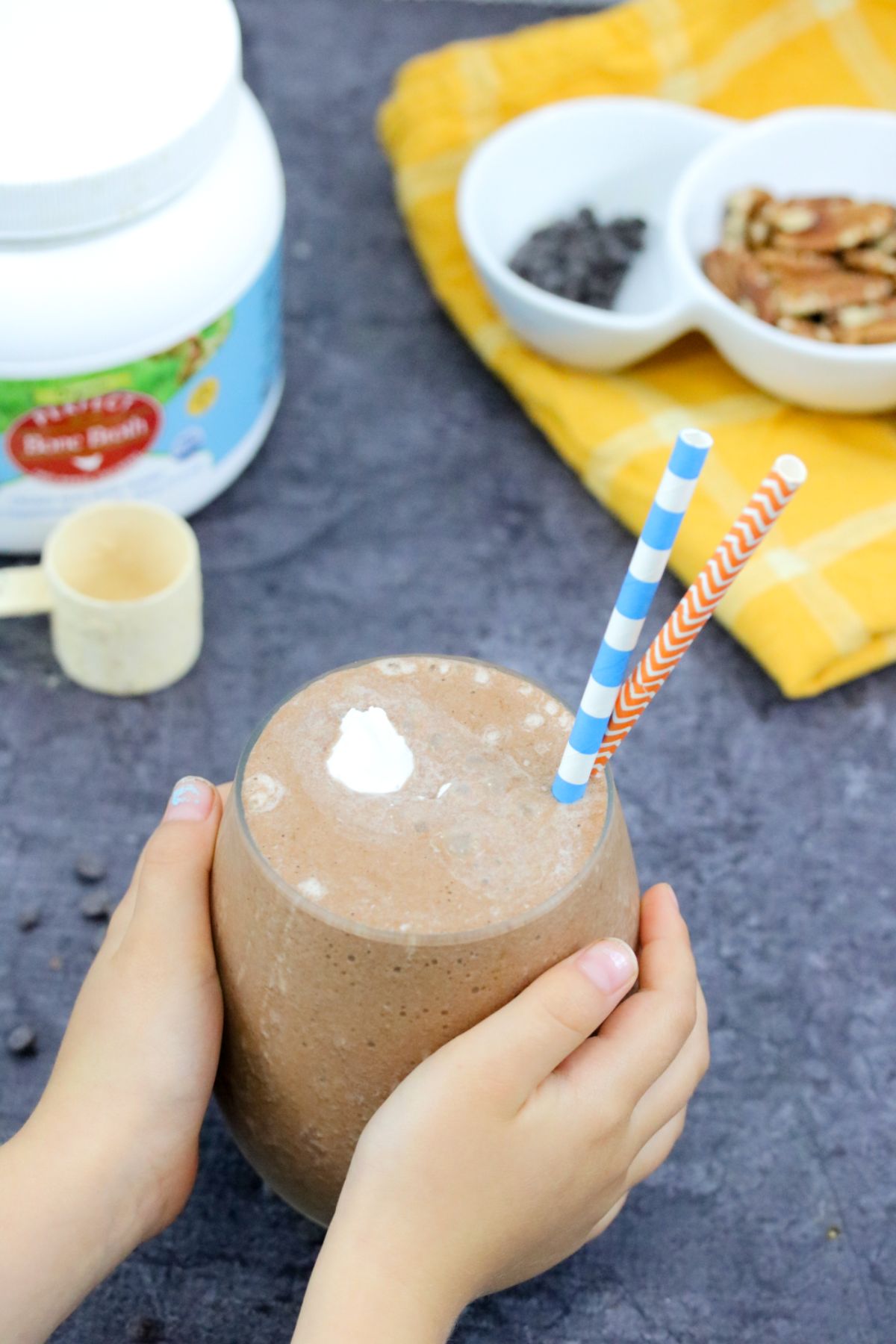 : vegan chocolate smoothie in a glass with toddler hands holding it.