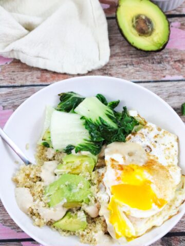 White bowl with quinoa, avocado, over easy eggs, and bok choy with avocado behind it