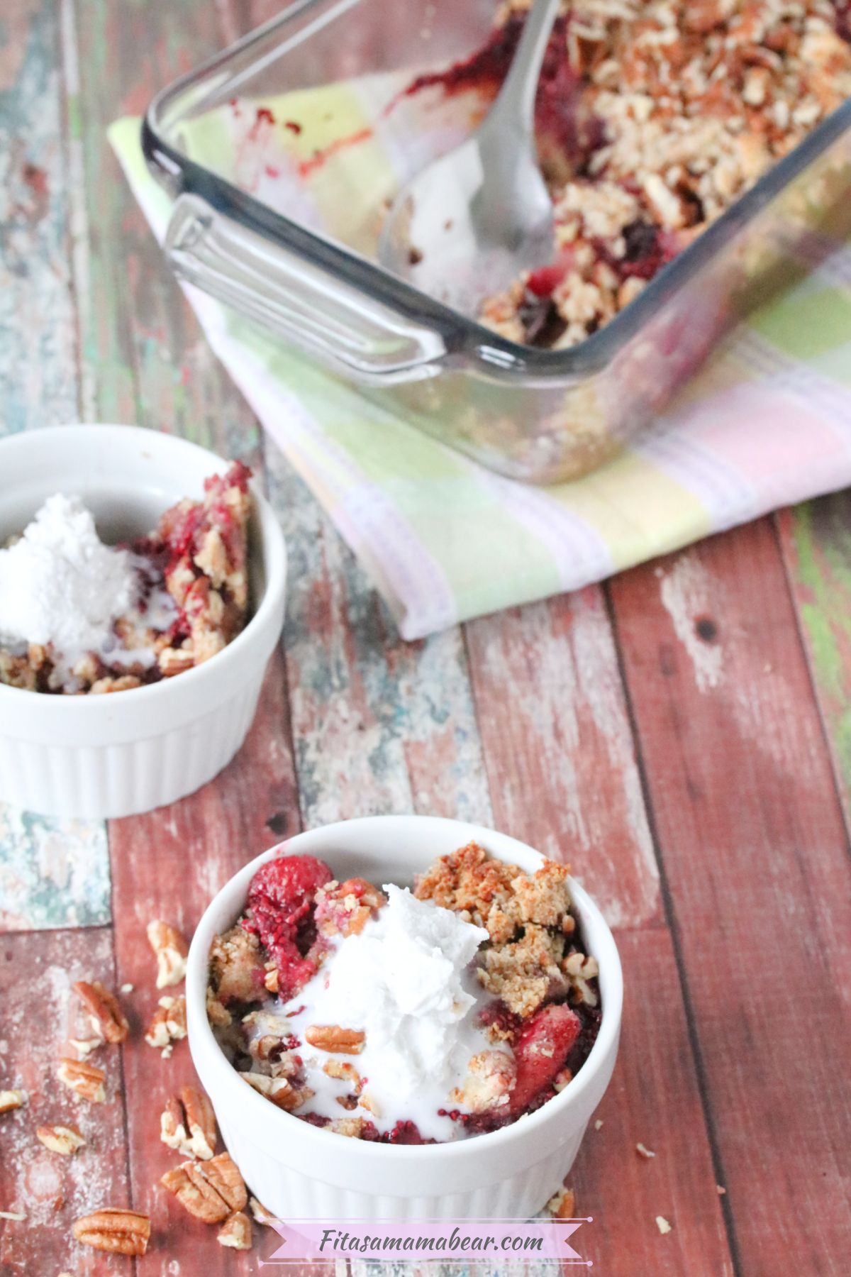 Paleo berry crumble in a white ramekin with pecans around it and more crumble behind it.