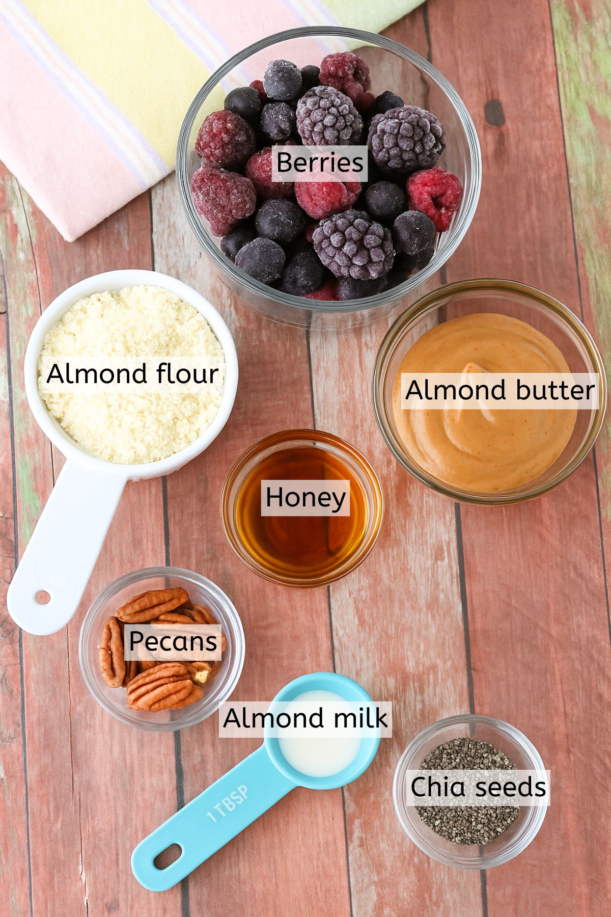Multiple ingredients like almond butter, chia seeds, frozen berries, and almond flour in cups with text labels over top.