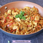 Featured image: healthy tofu scramble with red peppers, topped with parsley in a pan with a wooden spoon