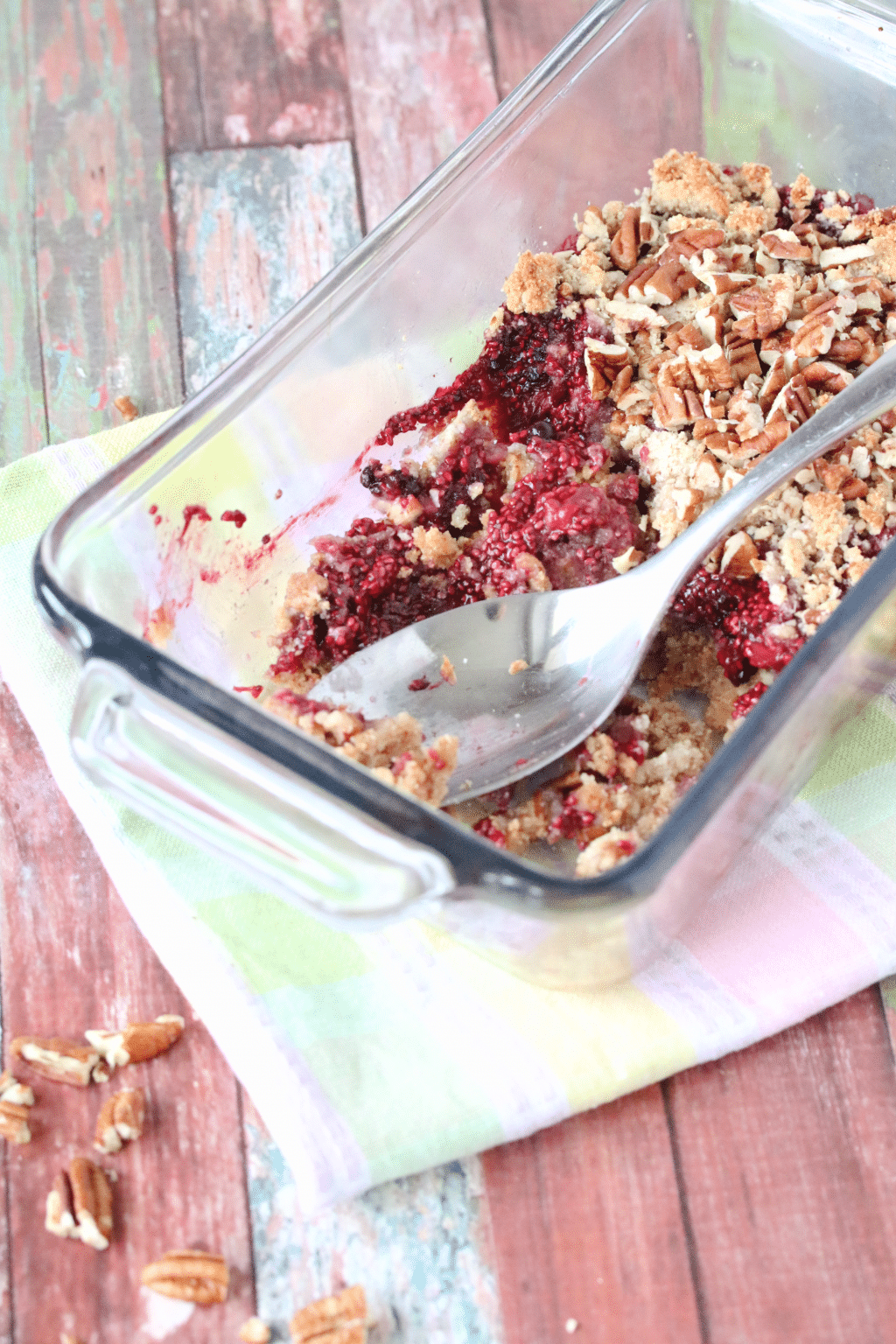 healthy berry crisp in glass dish with a spoon on a colored napkin