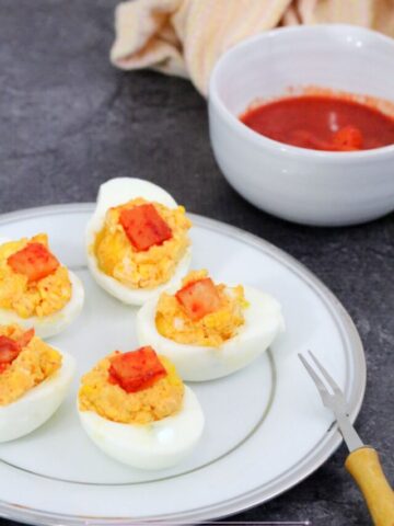 Deviled eggs with kimchi on top on a white plate with kimchi in a white bowl behind them