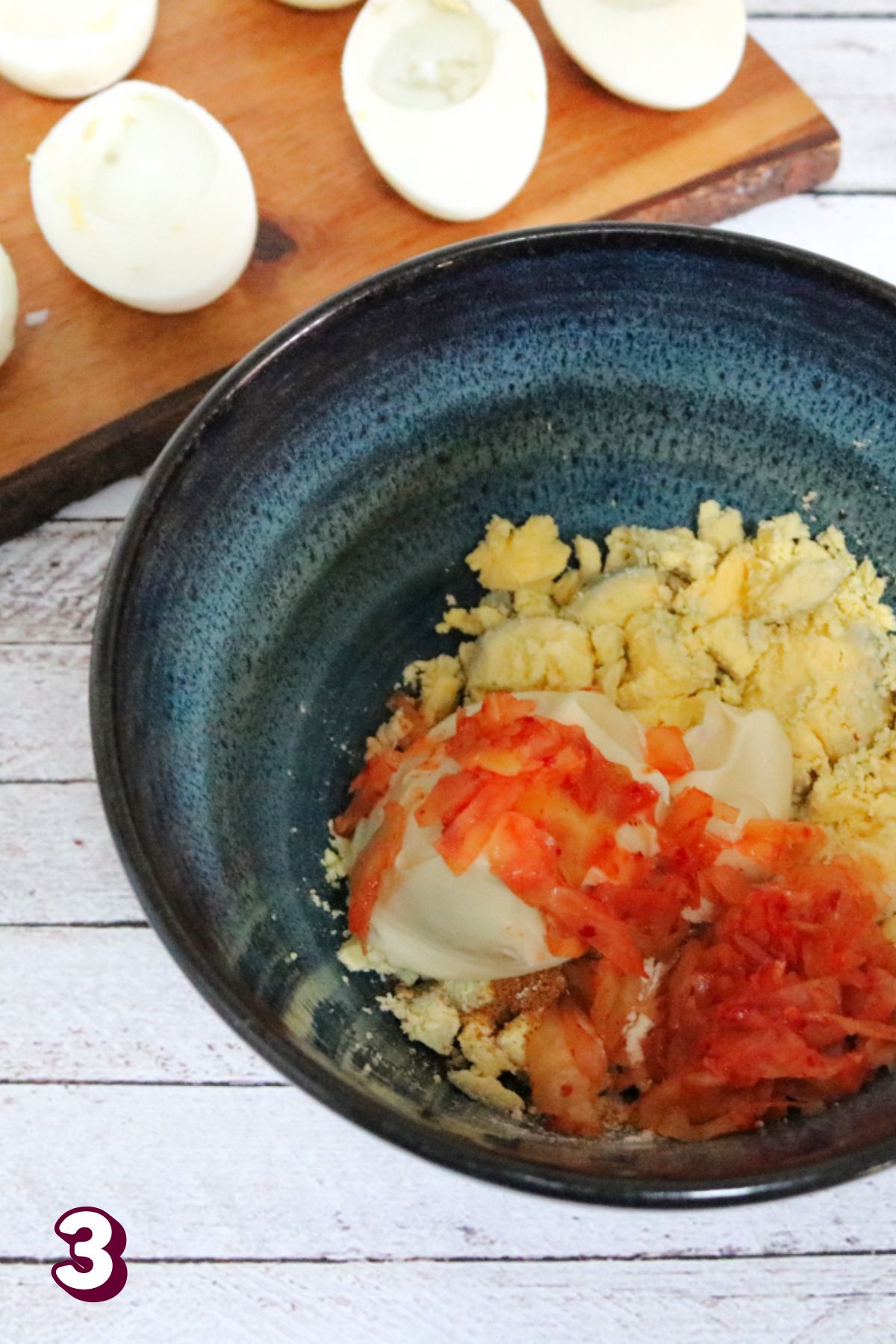 Blue bowl with boiled egg yolk and kimchi in it with hardboiled eggs behind it.