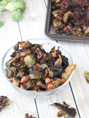 glass bowl with roasted brussels sprouts and more sprouts on a baking tray behind it