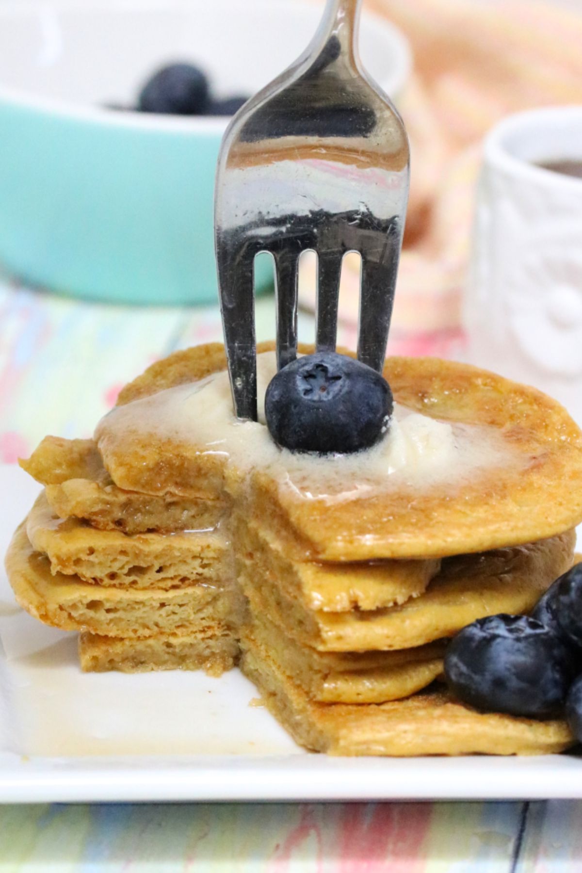 five banana-free protein pancakes stacked with blueberries beside them and butter on top with a fork stuck in them.