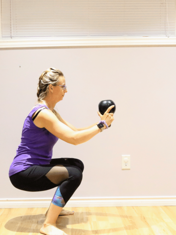 Woman in purple shirt and black pants performing a squat with a kettle bell
