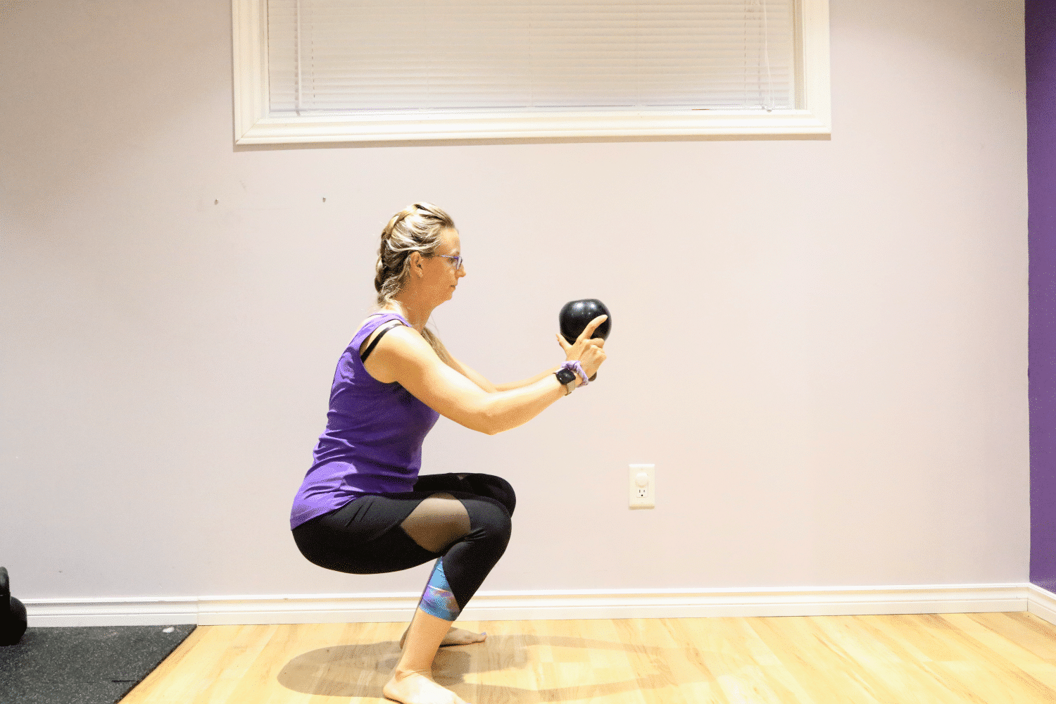 Woman in purple shirt and black pants performing a squat with a kettle bell
