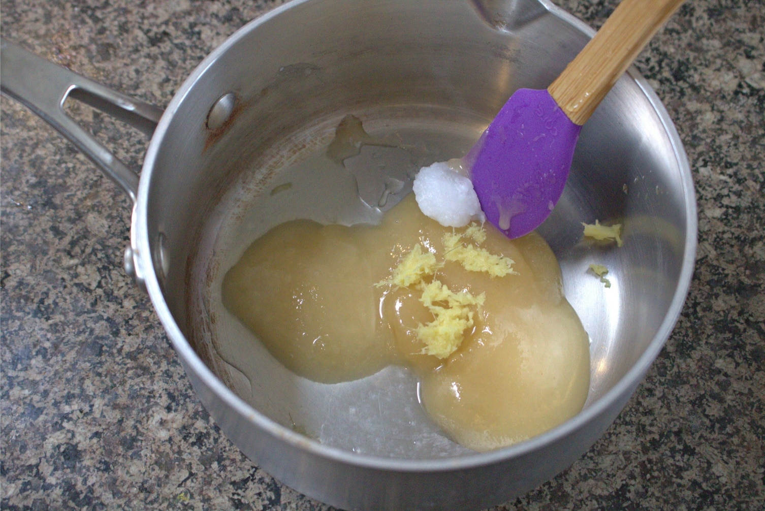 Small pot with honey and coconut oil with a purple spatula in it