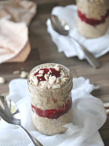 Two mason jars on top of white cheesecloth filled with peanut butter overnight oats and topped with jam