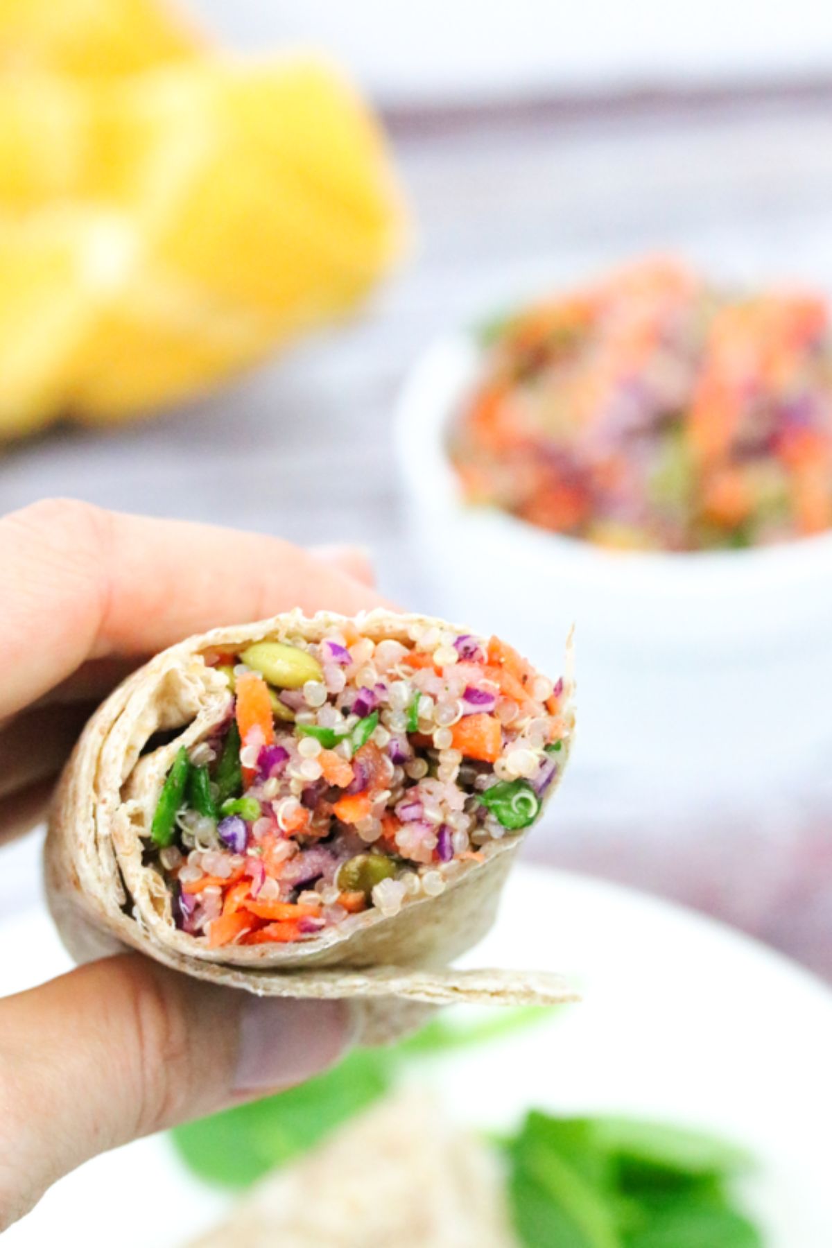 Hand holding up a quinoa salad wrap in half.