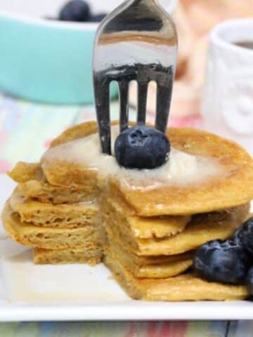 five banana-free protein pancakes stacked with blueberries beside them and butter on top with a fork stuck in them