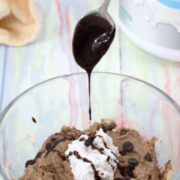 Spoon dripping chocolate onto a glass bowl of chocolate protein fluff topped with coconut whipped cream.