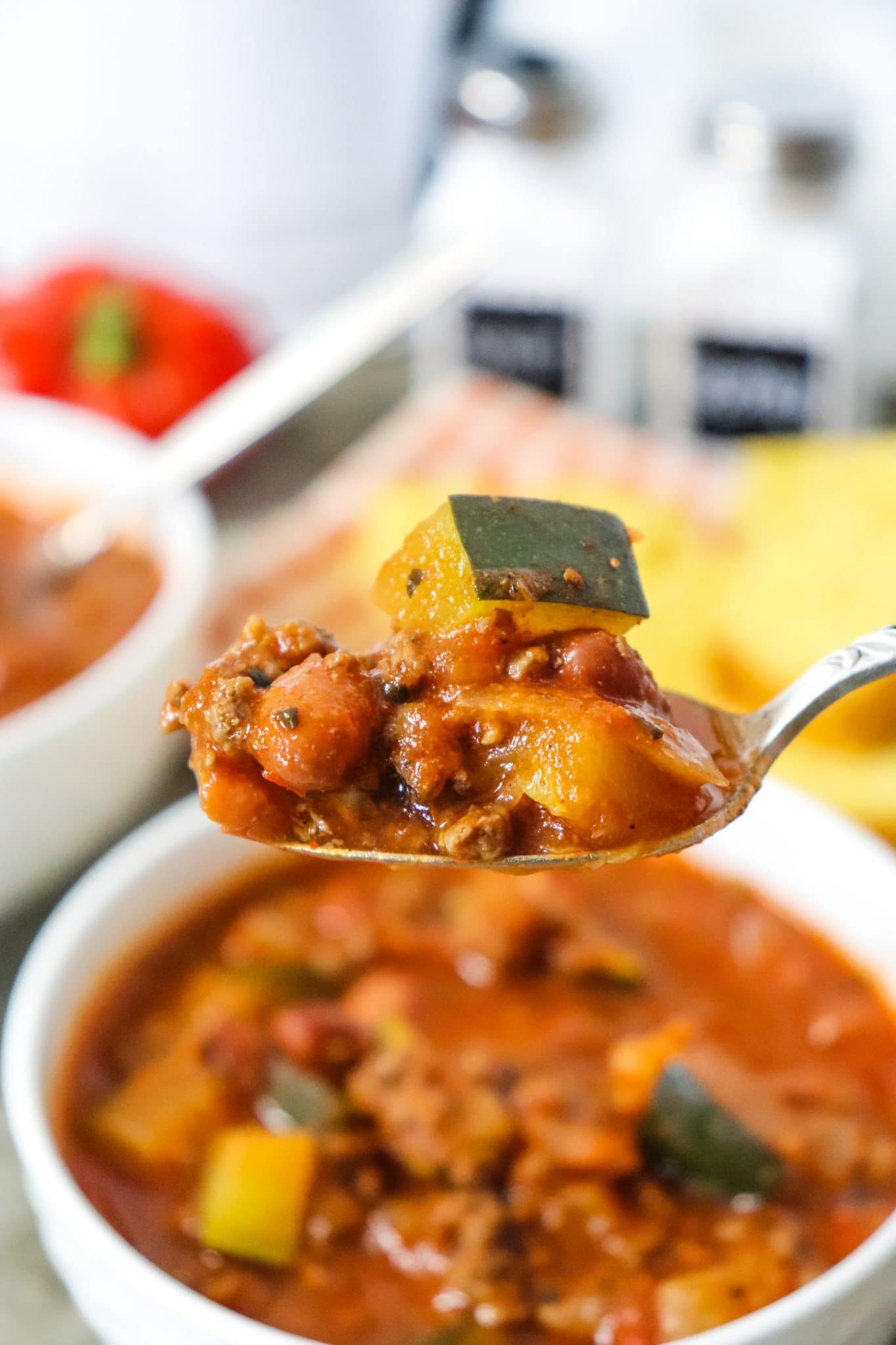 healthy chili dinner in a white bowl with spoon pulling out and another bowl and ingredients behind it