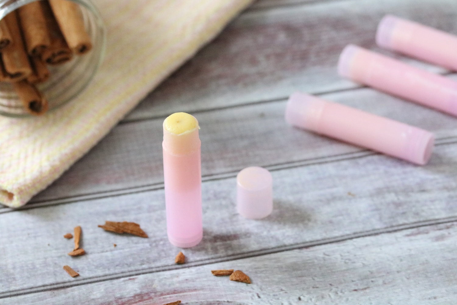 Pink lip balm tube with more behind it and pieces of chopped cinnamon sticks around it