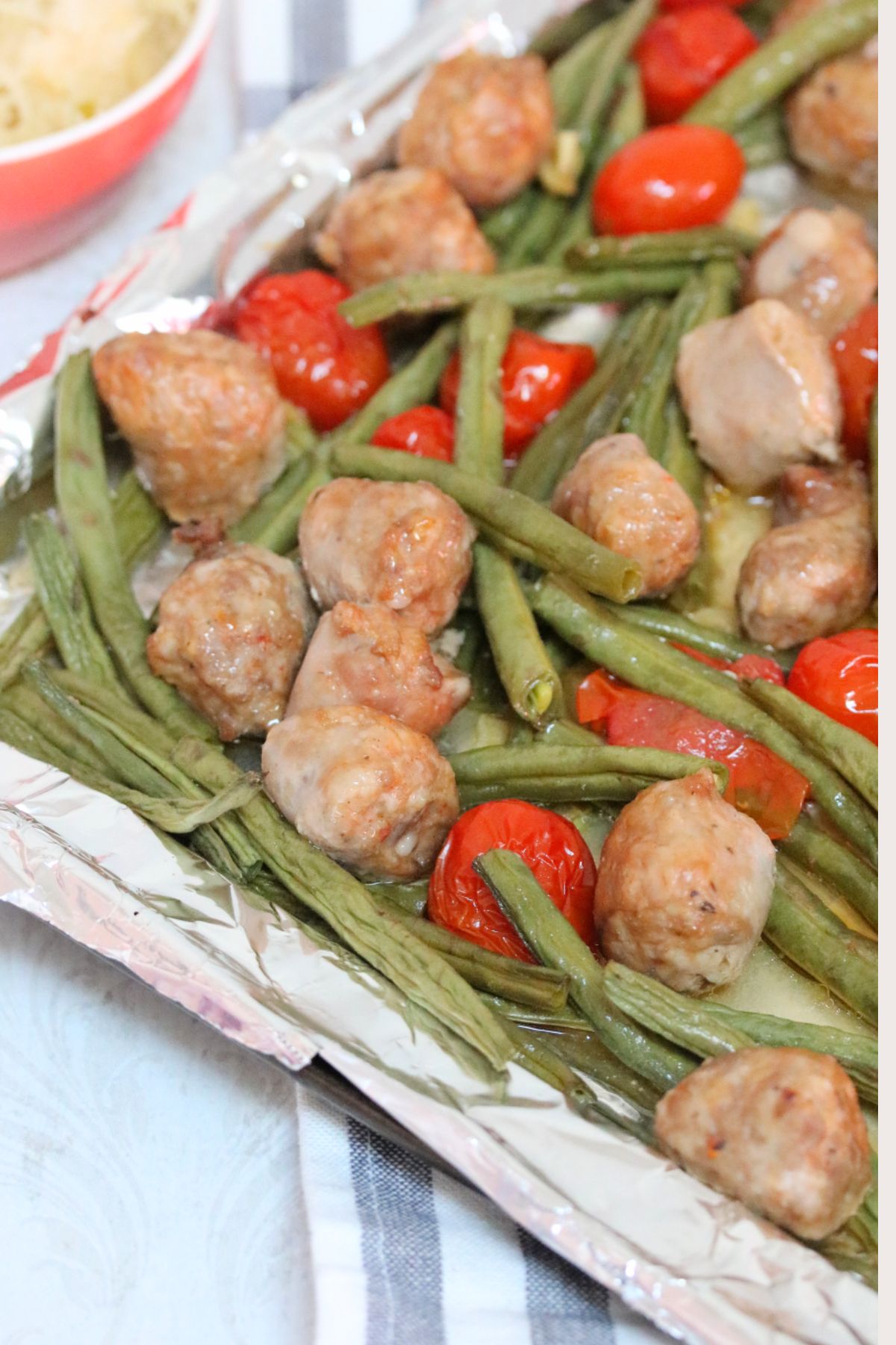 Sausage, green beans, cherry tomatoes, on a sheet pan with sauerkraut beside it.
