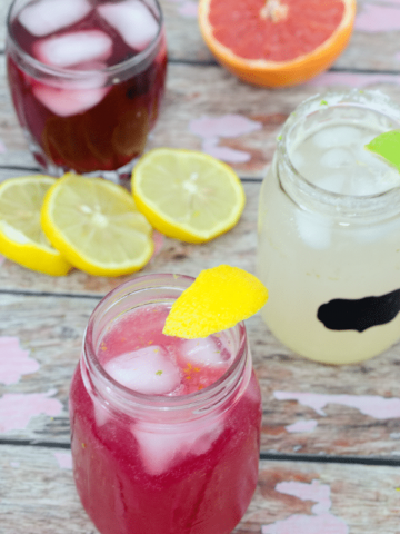 Three glasses with brightly colored non-alcoholic drinks with slliced citrus fruit around them
