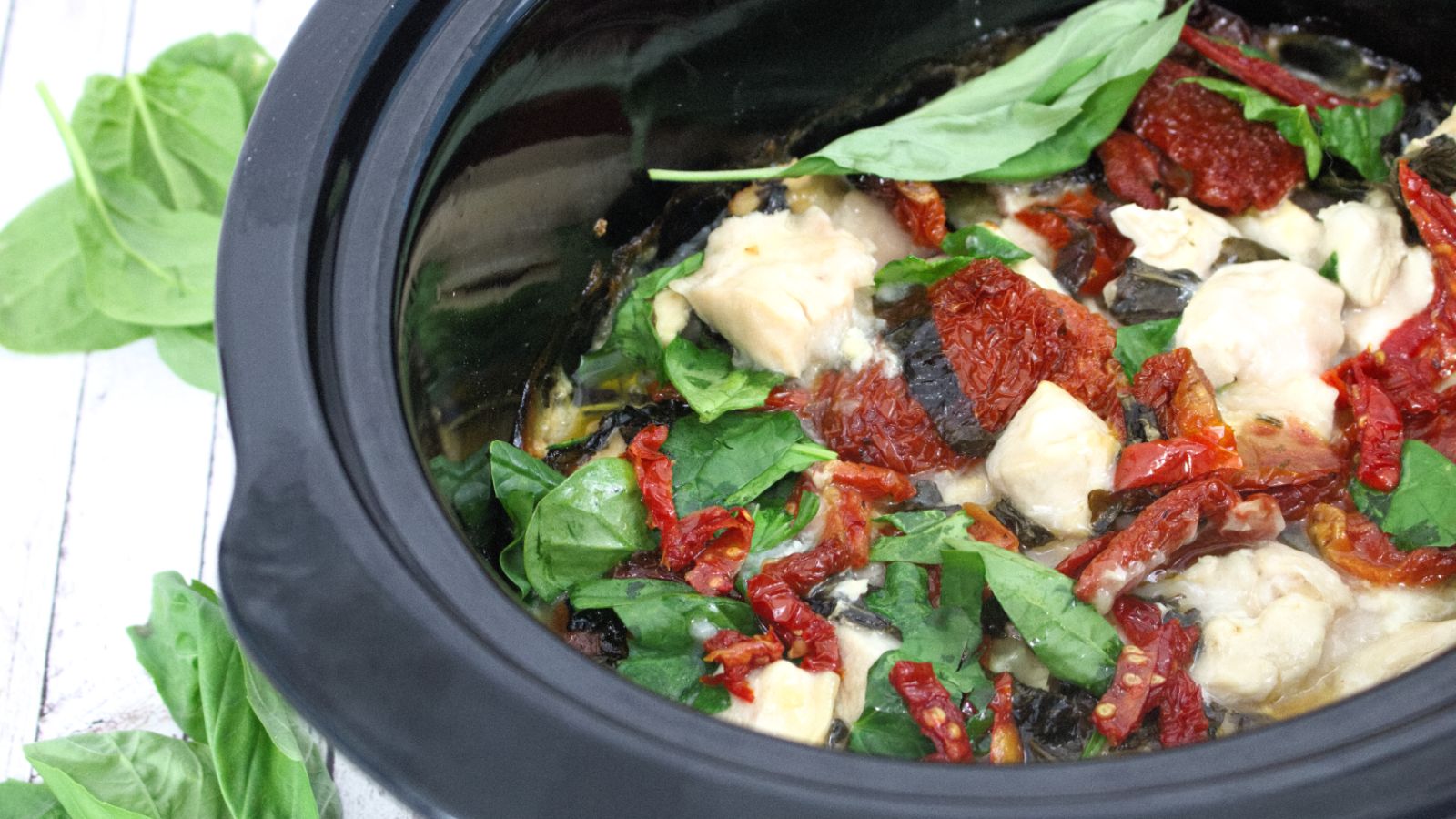 Sundried tomatoes, spinach, and chicken in a black slow cooker.