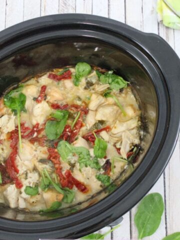 Tusccan chicken with spinach and sundried tomatoes in a cream sauce in a black slow cooker.