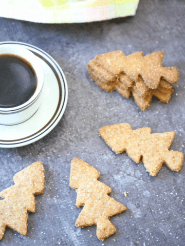 Three almond flour sugar cookies around a cup of coffee on a saucer with three more cookies stacked