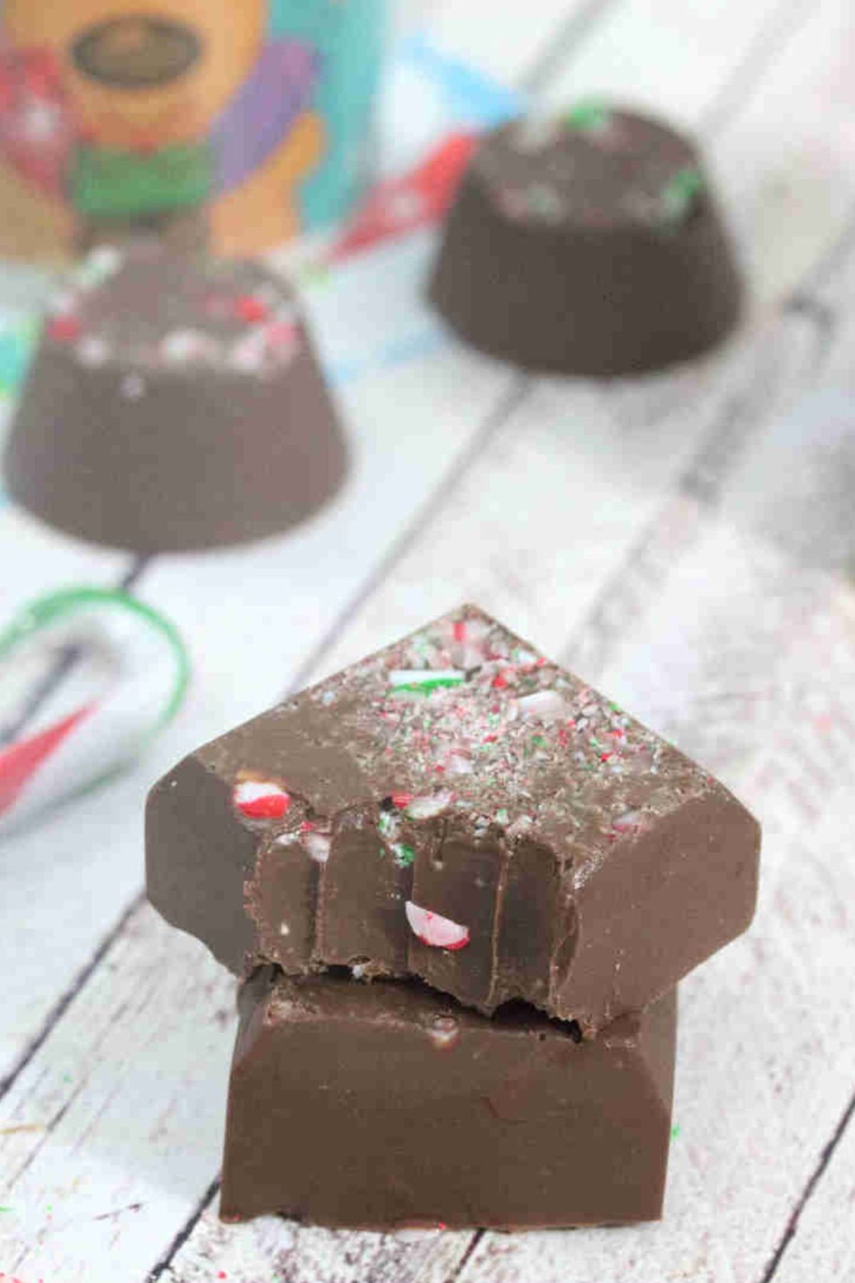 Two pieced of candycane fudge stacked the top with a bite out of it and more fudge and candy canes behind them.