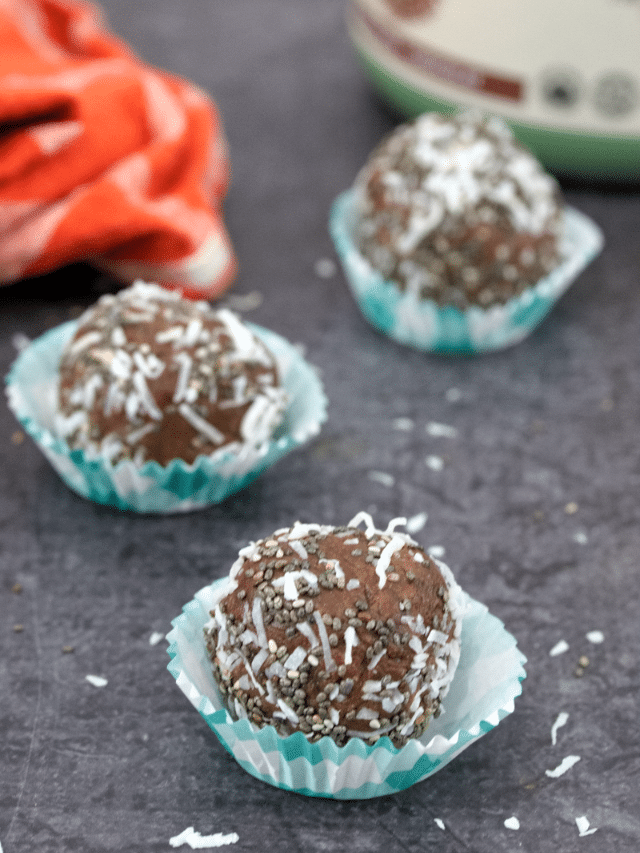Featured image of three chocolate protein balls in blue cupcake liners with more on an orange linen behind them and a tub of protein powder