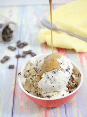 Ice cream in a red bowl with homemade peanut butter magic shell being poured on top and a yellow napkin behind it
